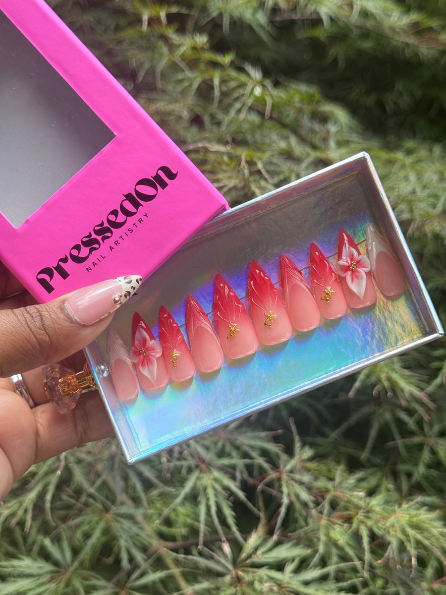 Set of medium-length stiletto press-on nails with a red ombre effect, accented with small gold stars and delicate white floral designs.