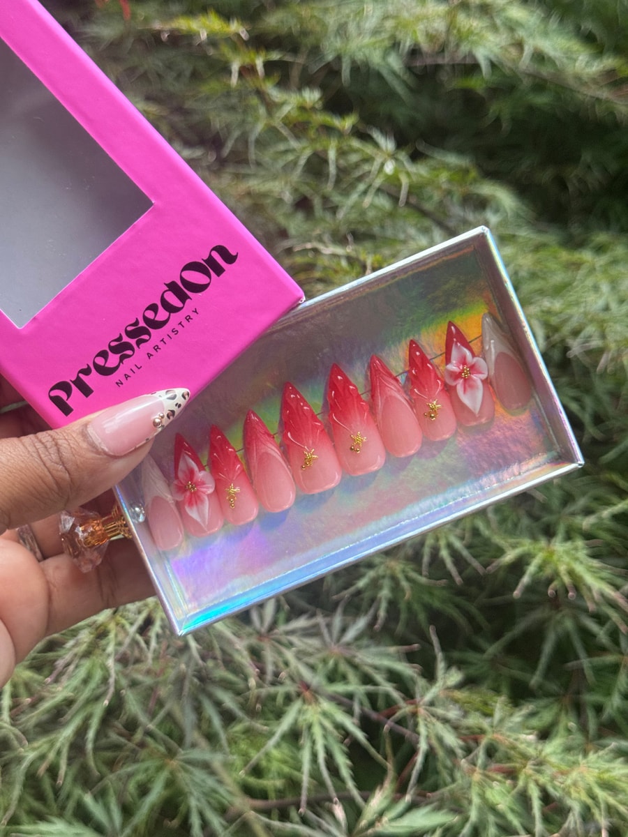 Red ombre medium press-on nails are embellished with delicate white flower accents and small gold details.