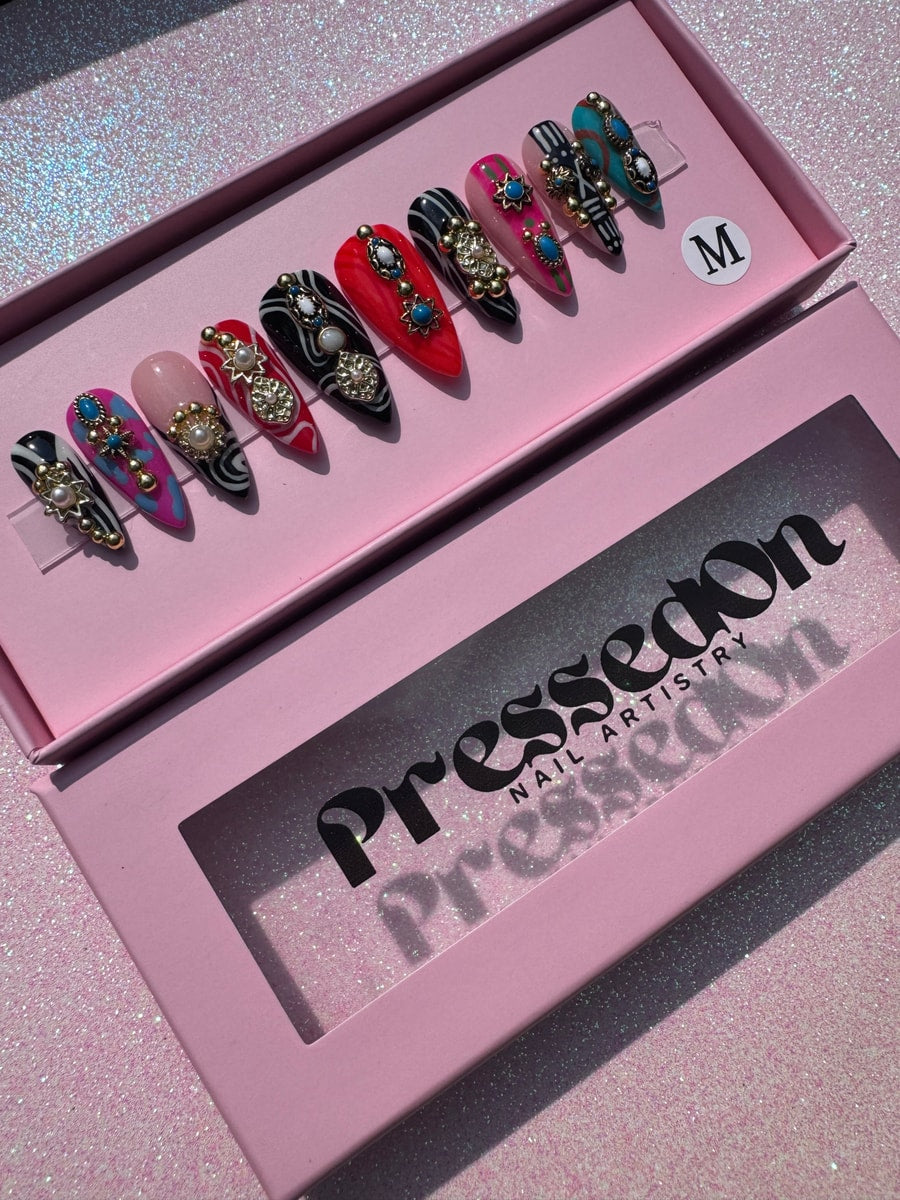 Set of short press-on nails with mixed patterns, gemstones, and pearls. Various nail designs include black and white stripes, red with white swirls, pink and blue leopard print, and turquoise.