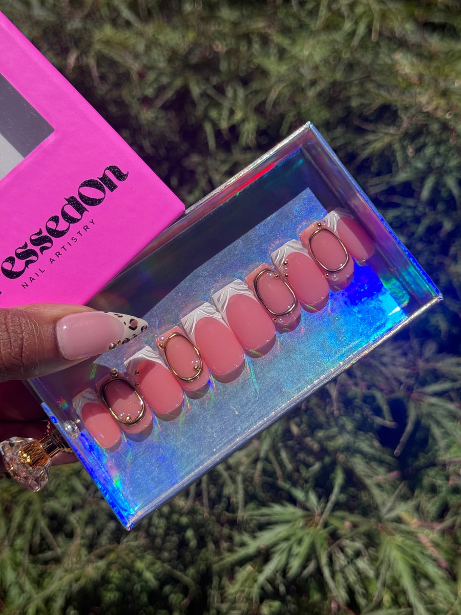 Set of short pink press-on nails with white French tips and gold oval decorations. Some nails have pearl embellishments.