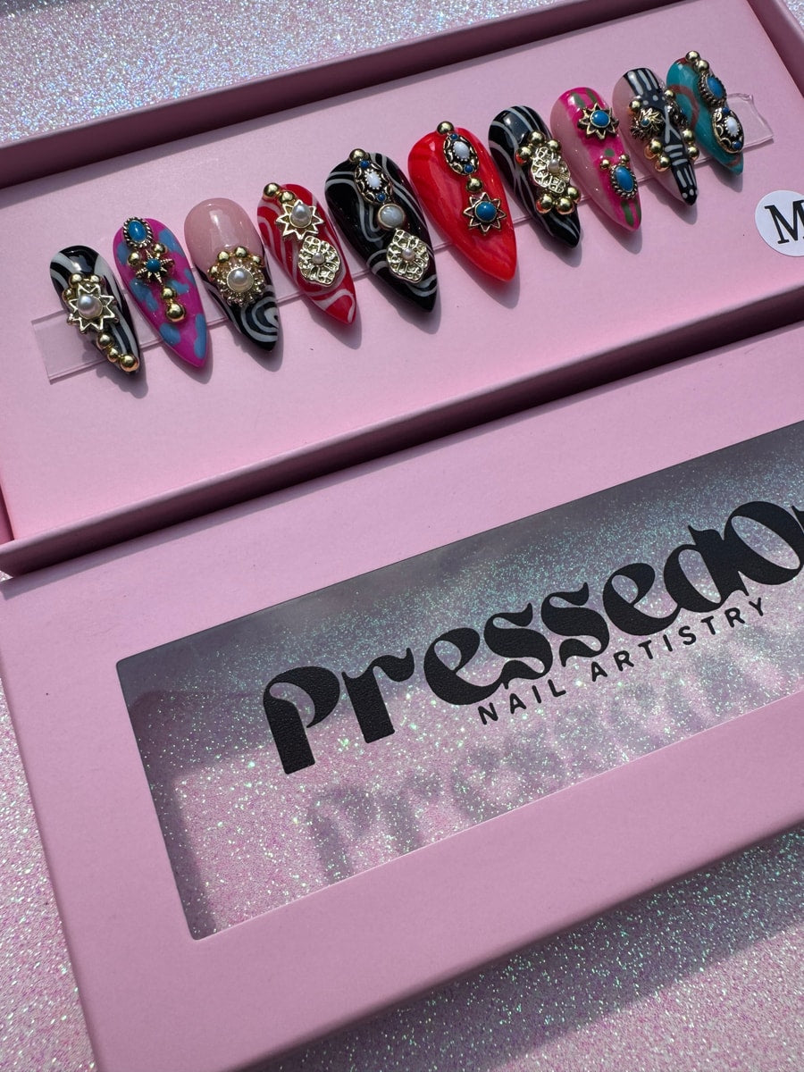 Assorted set of short press-on nails. Designs include zebra stripes, swirls, and colorful abstract patterns. Each nail is decorated with a gold charm and a pearl or turquoise stone.