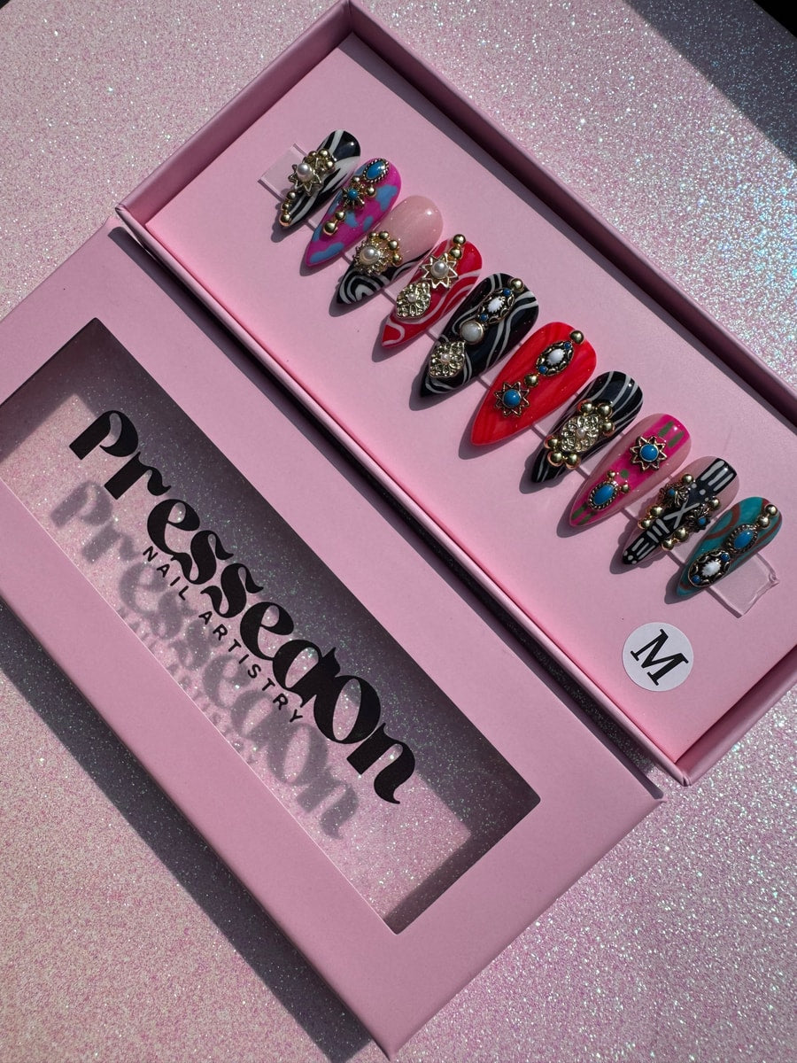 These are short press-on nails in a junk style with bold designs and gemstones. Nails include zebra stripes, bright colors, gold details, and various embellishments.