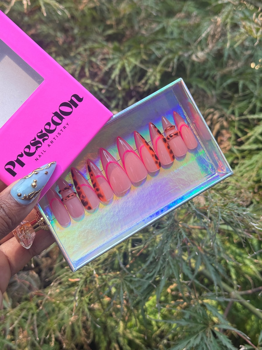 Pink short press-on nails feature a neon pink outline and a brown and orange animal print design. Some nails are decorated with gold rings.