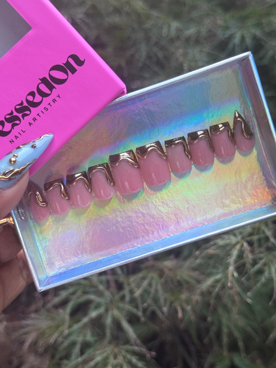 Short pink press-on nails feature gold dripping accents around the tips. 