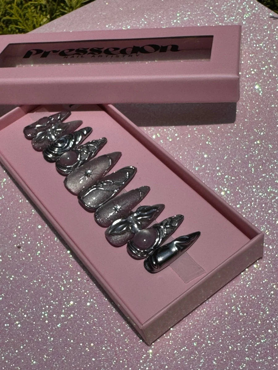 Medium length chrome press-on nails feature swirling 3D silver decorations and a pink stone on select nails.