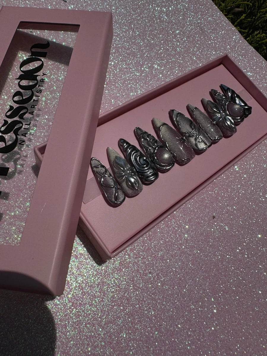 Medium length chrome press-on nails featuring metallic silver embellishments and 3D sculptural decorations, including flower, swirl, and orb accents.