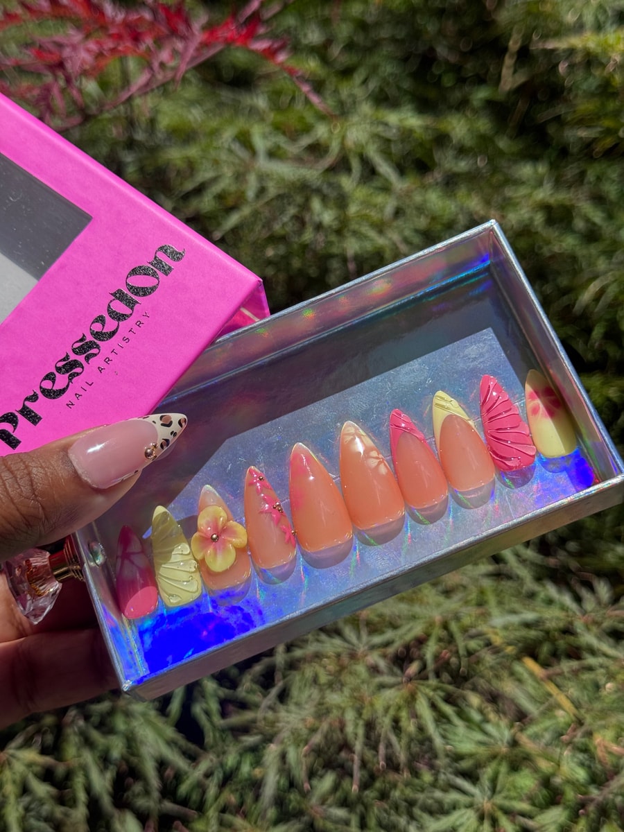 Short, stiletto press-on nails in a springtime theme featuring pink, yellow, and peach tones, with floral accents and french tips.