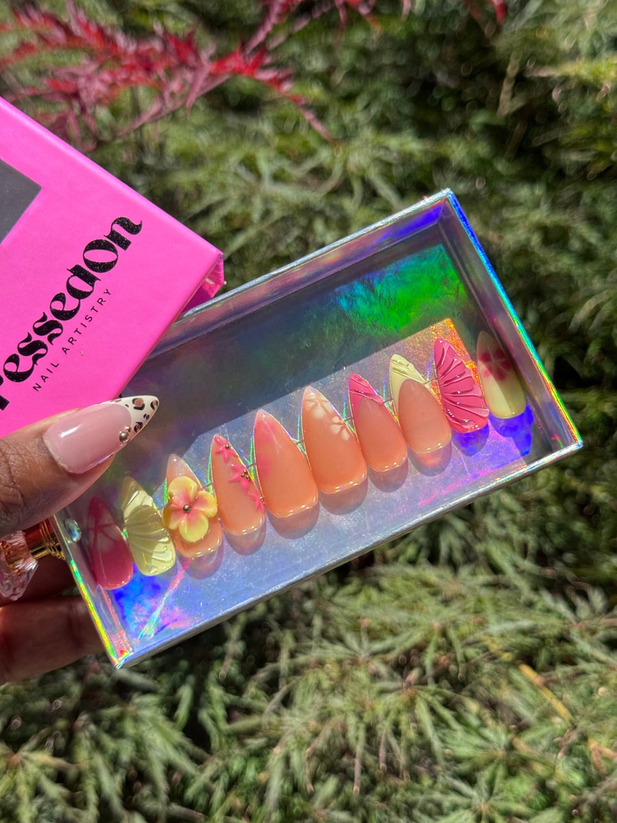 Short almond press-on nails featuring floral designs, butterfly accents, and pastel pink and yellow colors for a springtime vibe.
