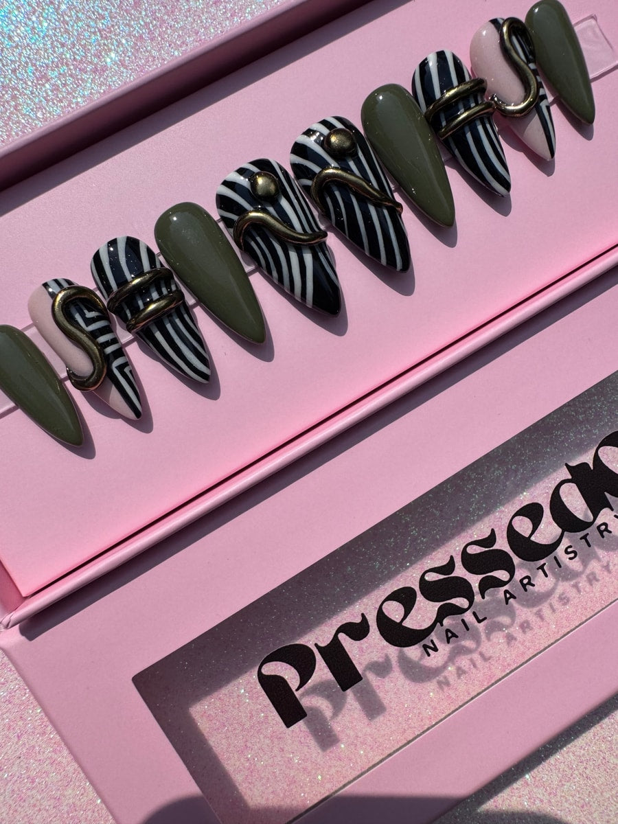 Set of stiletto press-on nails with geometric designs, including zebra stripes, olive green, and pale pink, accented with a raised gold serpentine design.