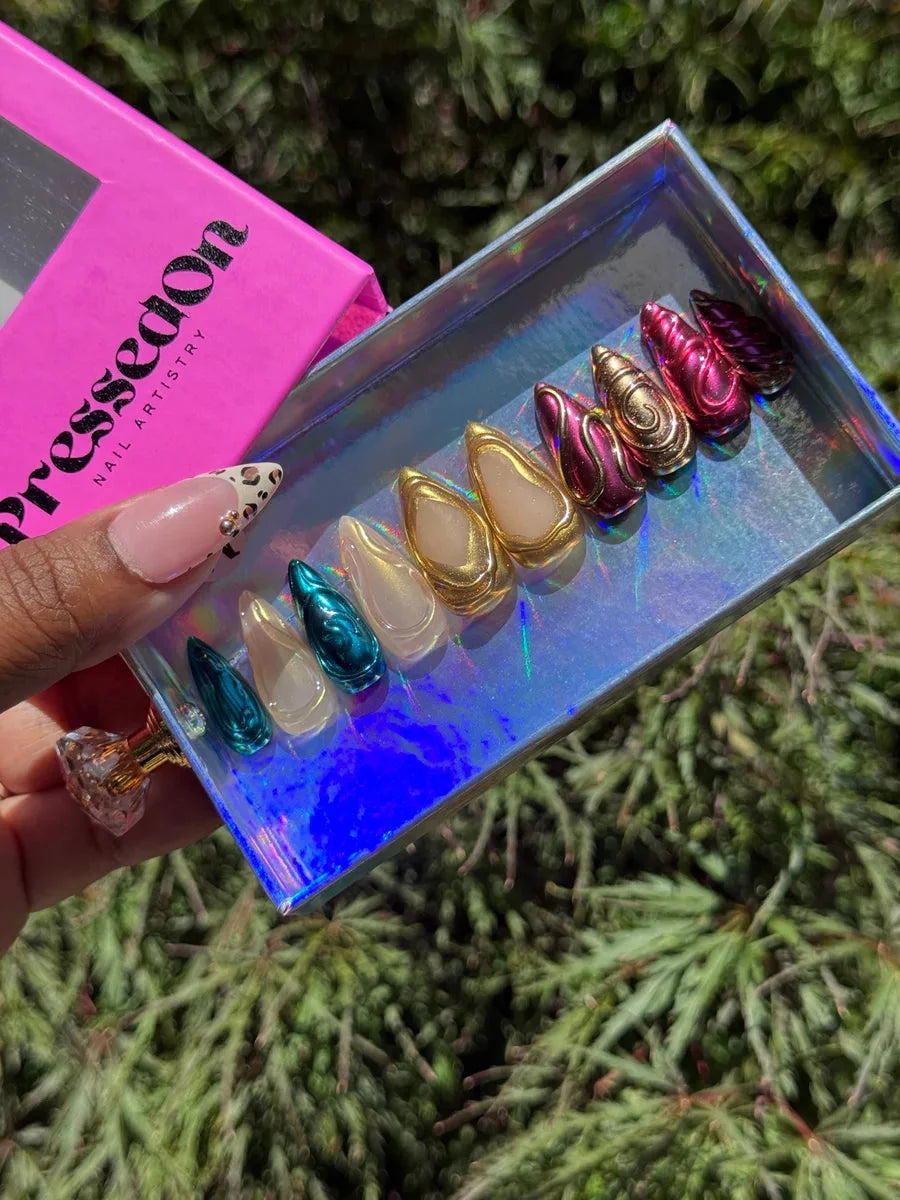 Assorted short stiletto press-on nails with chrome finishes in teal, gold and pink with unique 3D designs.