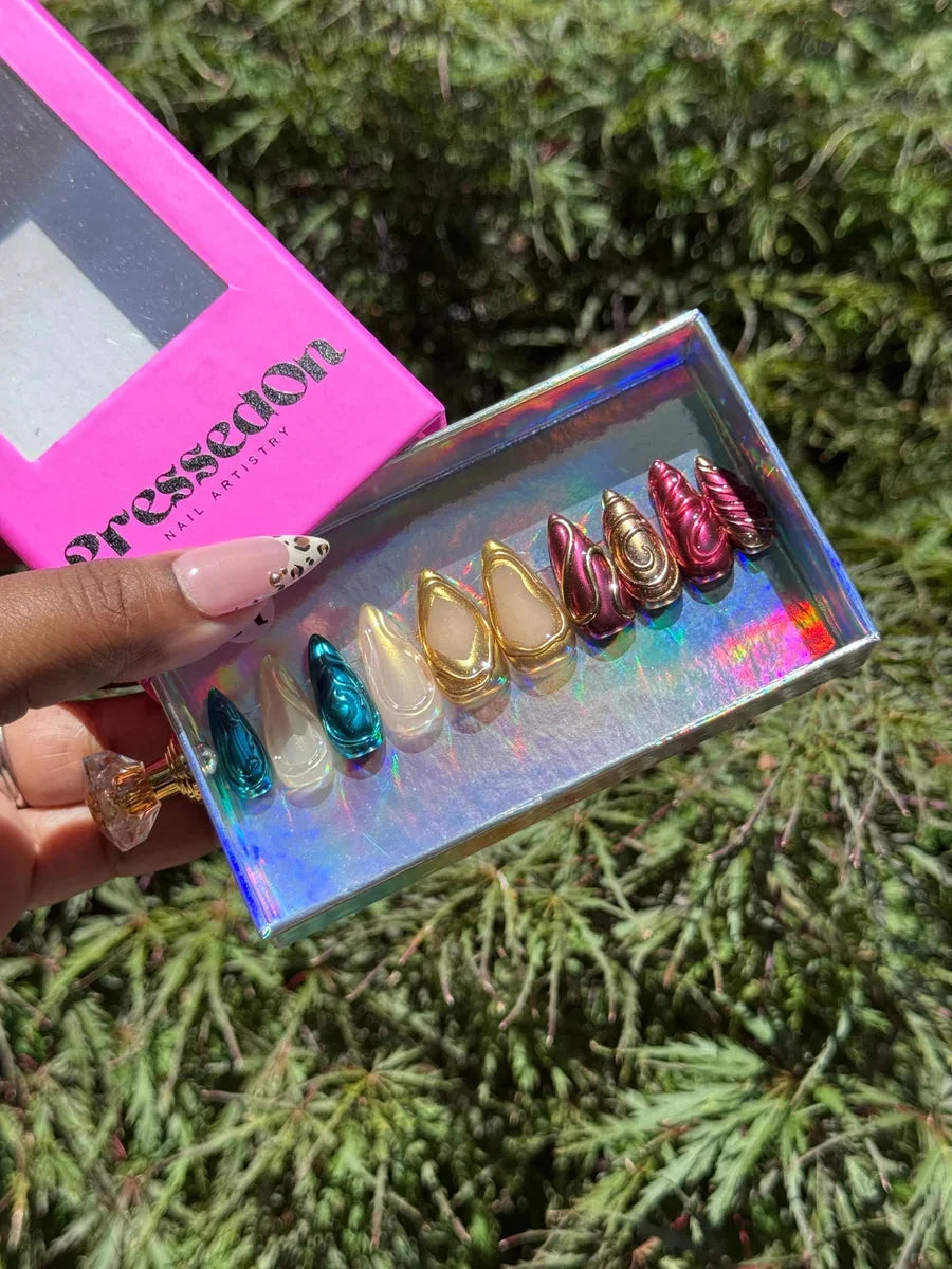 Assorted short press-on nails with chrome finishes and 3D designs in teal, gold, pink, and nude with animal print.