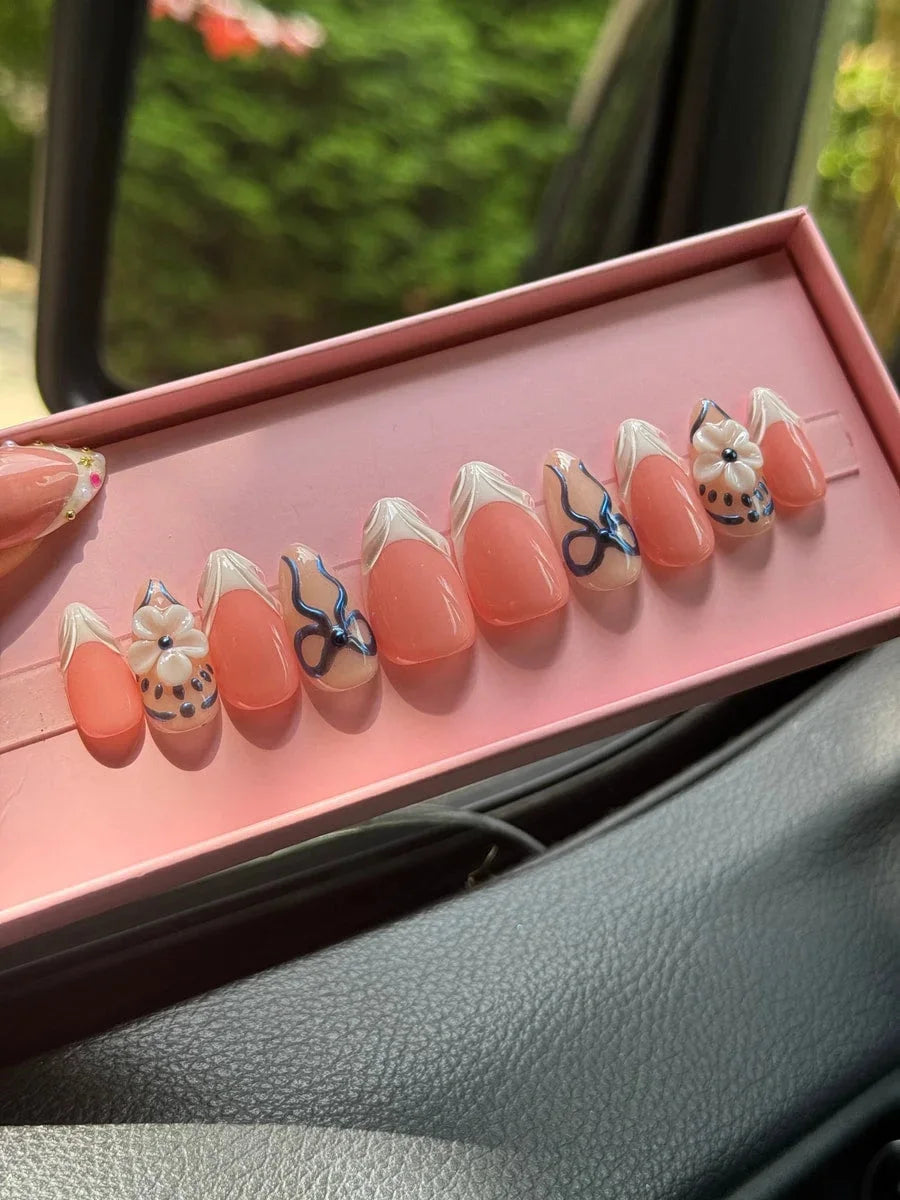 Super short press-on nails with a peach base and white French tips. The nails feature a blue chic design with delicate bow accents and 3D flower nail charms.