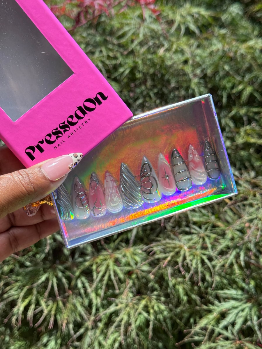 Medium unicorn press-on nails are decorated with abstract silver wire art on a pale pink and white background.