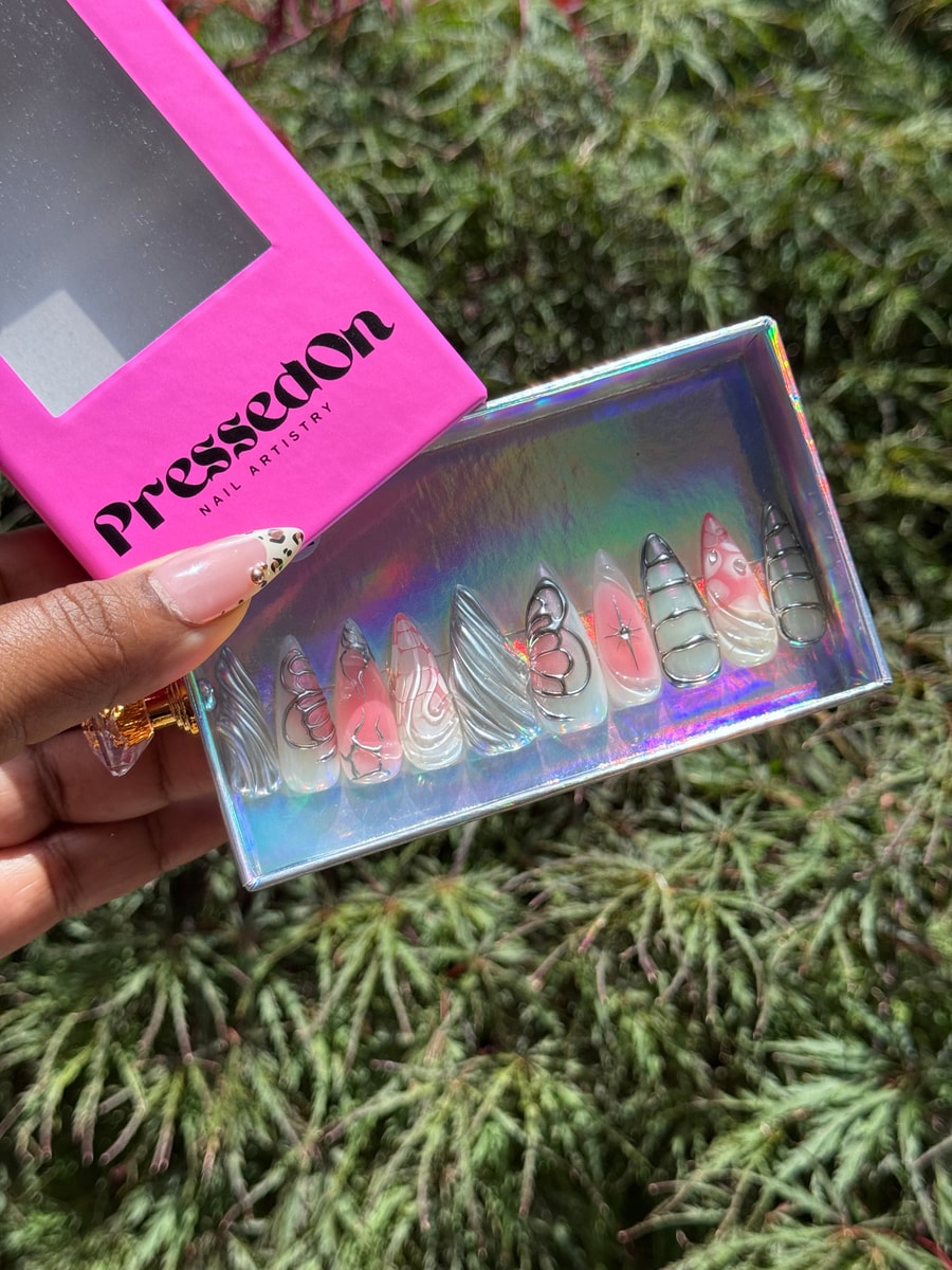 Set of medium-length unicorn press-on nails features clear and light pink shades with unique swirling silver chrome designs and other delicate embellishments.