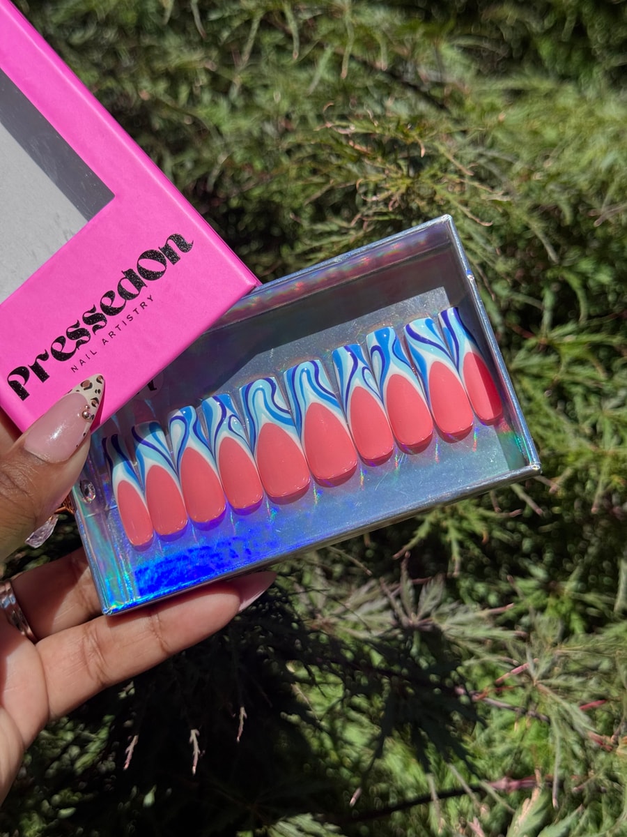 These are medium length press-on nails featuring a coral pink base with a wavy blue and white swirl design. The set has a glossy finish.