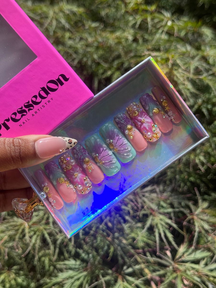 These medium press-on nails have a whimsical design featuring pastel shades, floral accents, pearls, and gold charms.
