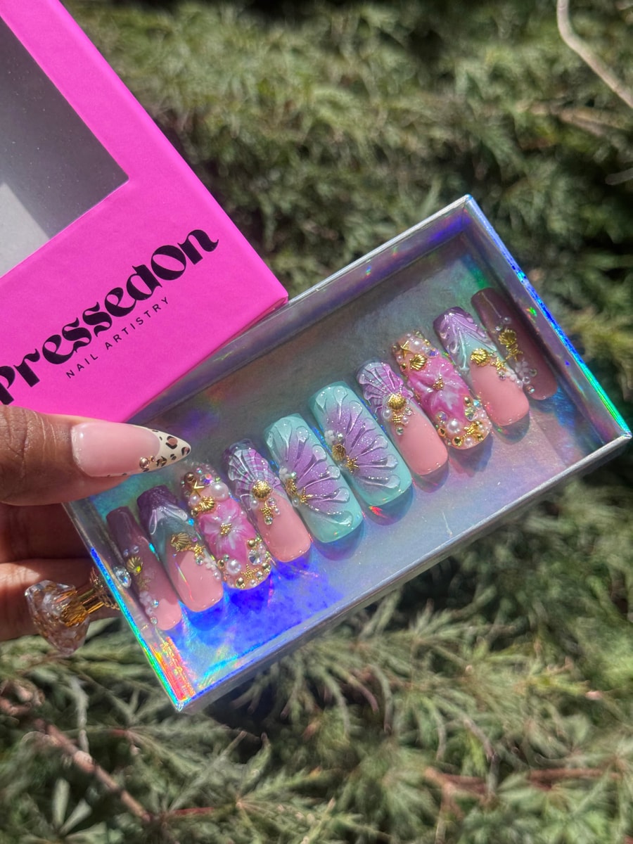 Medium press-on nails with a whimsical floral and seashell design in pastel pink, blue, and purple, adorned with pearls and gold.