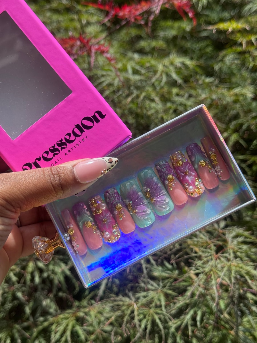 Set of whimsical medium-length press-on nails featuring pink, purple, and turquoise colors. The nails are decorated with seashell accents, pearls, and small rhinestones.