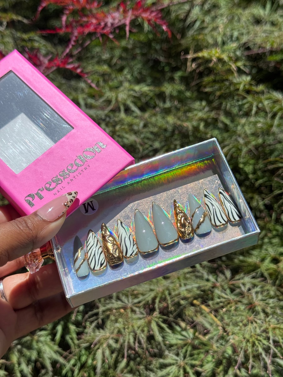 A set of medium-length stiletto press-on nails features zebra print, chrome, and gold accents.