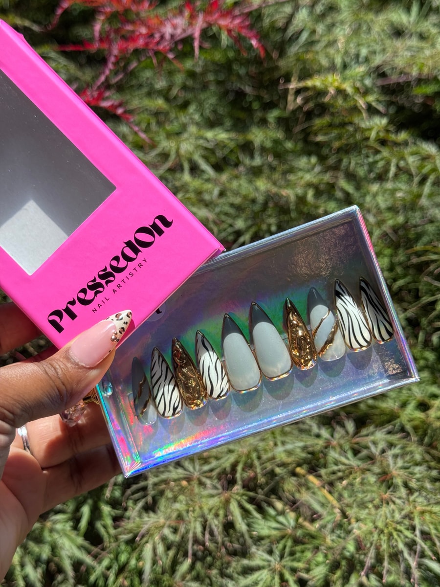 A set of medium-length press-on nails with zebra stripe designs, chrome accents, gray, and gold details. The set includes a mix of glossy and textured nail designs.