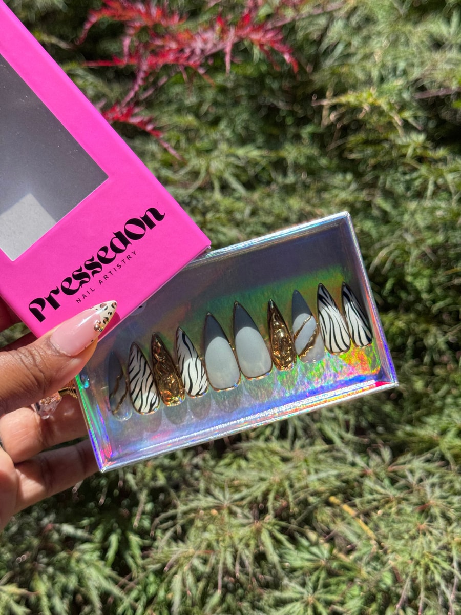 This is a set of medium stiletto press-on nails with zebra stripes, chrome finish, and gold accents. Some nails are zebra patterned, while others are chrome or gold.